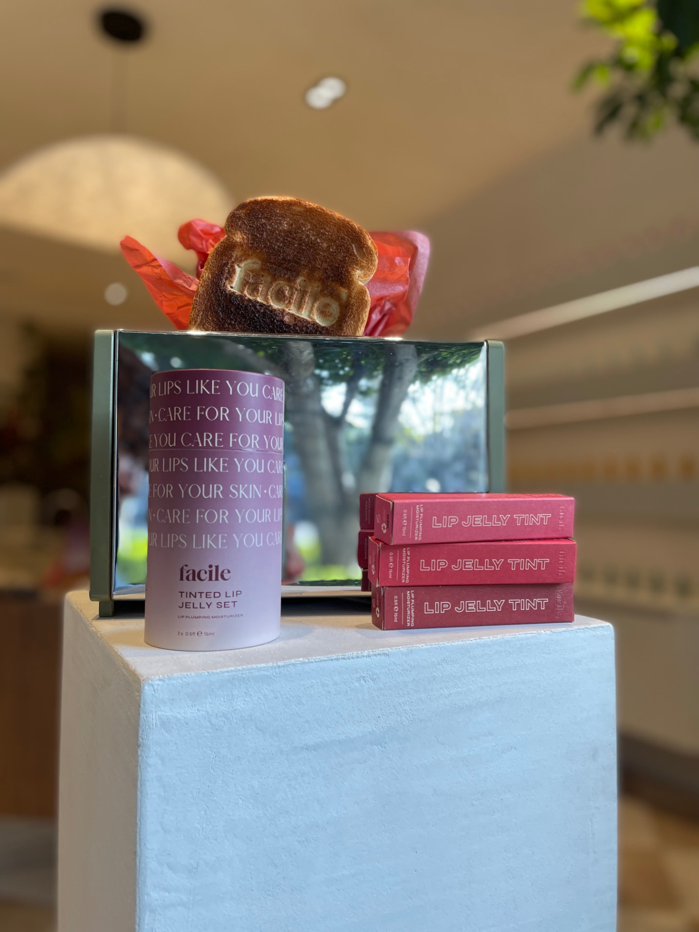 A slice of toast branded with the Facile logo, styled with Tinted Lip Jelly packaging in front of a mirror