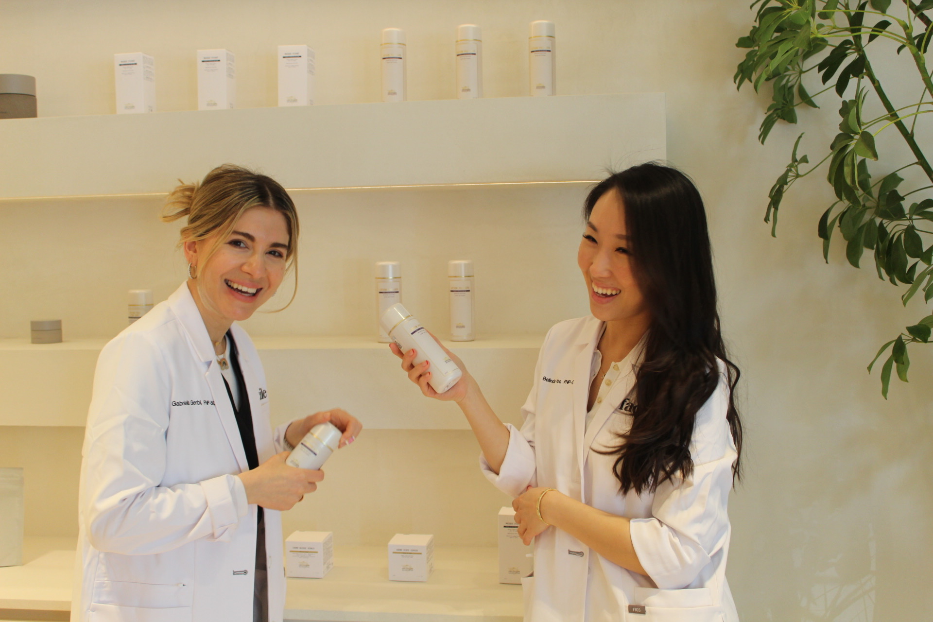 Two Facile estheticians laughing while holding product in front of the retail shelving