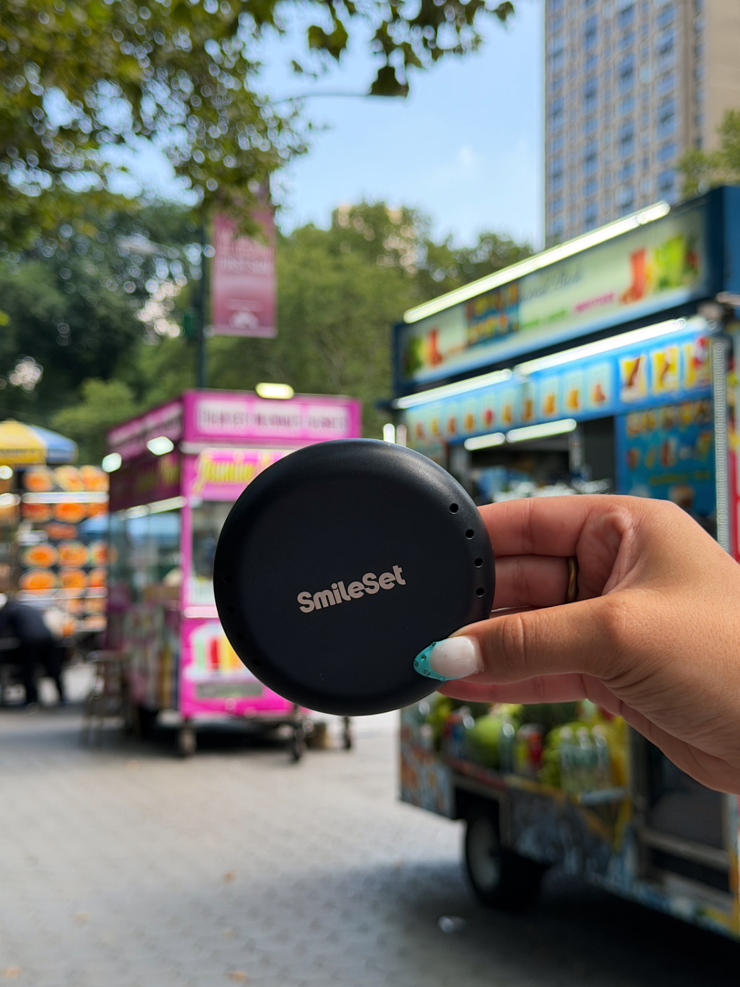 SmileSet aligner case held up along a Central Park path with food carts in the background