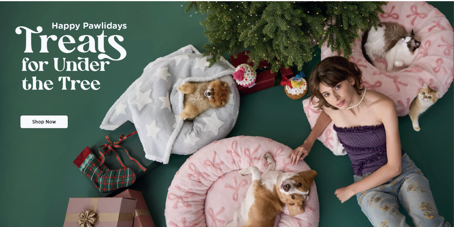 Lesure holiday campaign hero, model and pets styled among pink bow-print pet beds under a Christmas tree