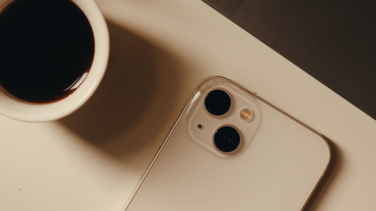 Phone and a cup of black coffee on a warm cream desk